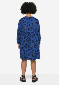 Robe bleue avec un imprimé léopard noir, manches bouffantes longues, taille froncée et coupe décontractée. Assortie avec des sandales noires à lanières.