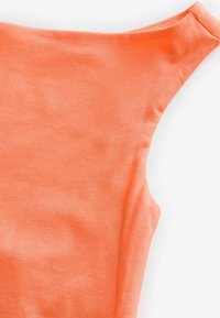 Oranssi lyhythihainen paita pehmeästä puuvillakankaasta, jossa on pyöreä kaula-aukko ja sileä pinta, näkyvät vain vähäiset ryppyjä.