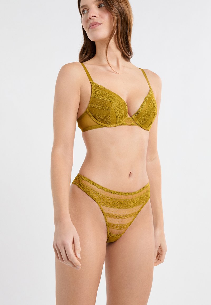 Ensemble de lingerie en dentelle vert olive comprenant un soutien-gorge rembourré avec bretelles ajustables et un slip taille haute assorti avec des accents transparents et des bords festonnés.