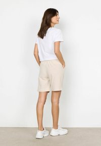 T-shirt blanc à manches courtes associé à un short beige clair avec une taille élastique et des poches latérales ; le modèle porte des baskets blanches.