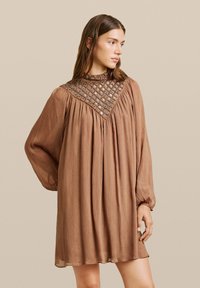 Vestido marrón de manga larga con un diseño plisado y un collar con patrones intrincados y acentos metálicos. Tejido suave y fluido con una textura lisa.