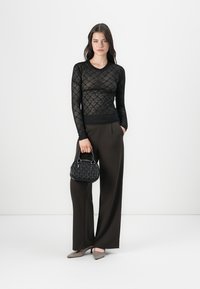 Haut en dentelle noire à manches longues, pantalons noirs taille haute, chaussures grises et un petit sac à main noir texturé avec des poignées rondes.