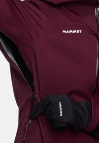 Vinröd vattentät jacka med dragkedja framtill, logotyp på bröstet och en ficka, tillsammans med en svart handske med samma logotyp.