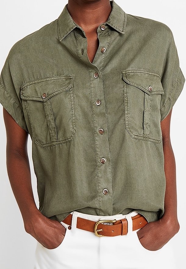 Personne portant une chemise kaki à manches courtes avec deux poches avant et un pantalon blanc avec une ceinture en cuir marron.