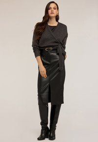 Pulover gri tricotat, fustă lungă din piele neagră cu slit frontal și cizme cu toc înalte din piele croc neagră până la genunchi.