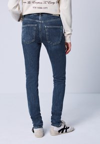 Kapeat farkut tummansinisestä denimistä, joissa on takataskut, keskipitkä vyötärö ja hienovarainen haalistuminen. Yhdistetty vaaleavärisiin lenkkikenkiin.