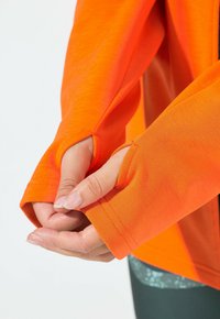 Oranžové sportovní tričko s otvory na palce v rukávech, které má hladkou tkaninu a detaily švů. Vyznačuje se živou barvou a funkčním designem.