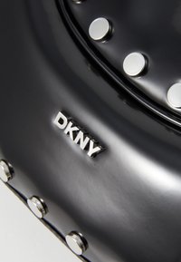Borsa nera con superficie liscia, dettagli in metallo argentato e logo "DKNY" in rilievo. Borchie circolari sono distribuite uniformemente lungo il bordo.