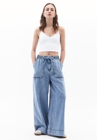 Vaaleat siniset leveälahkeiset farkut, joissa on elastinen vyötärö ja narun säätö, kahdella etutaskulla ja ompeluyksityiskohdilla varustettu helma.