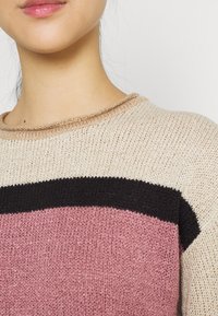 Maglione lavorato a maglia con scollatura rotonda, design a righe in beige, nero e rosa, con texture varie e vestibilità ampia.