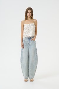 Light beige, textured tank top with spaghetti straps paired with high-waisted, wide-leg, light blue denim jeans and beige sandals.