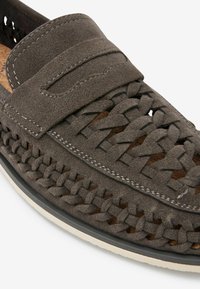 Gray suede moccasin-style shoe with woven detailing, slip-on design, contrasting stitching, and a light-colored rubber sole.