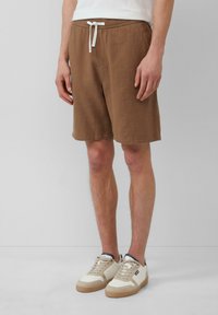 Shorts en tricot gaufré marron avec cordon blanc, poches latérales et coupe décontractée, associés à des baskets crème et beige.