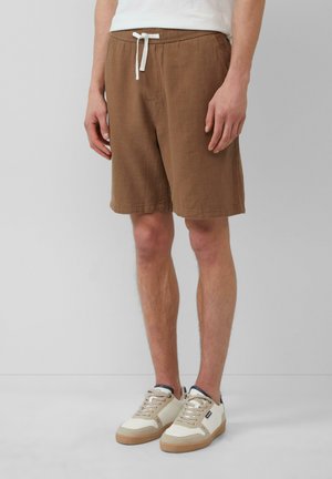 Shorts en tricot gaufré marron avec cordon blanc, poches latérales et coupe décontractée, associés à des baskets crème et beige.