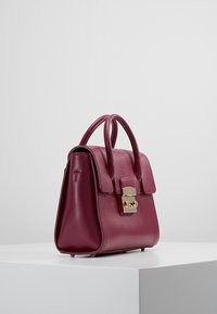 Burgunderfärgad läderhandväska med en strukturerad form, dubbla handtag upptill, guldfärgad detaljer och en slät textur. Inkluderar ett lock med överlapp.