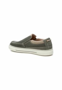 Zapatos slip-on de tela gris con una superficie texturizada, paneles laterales elásticos y una suela de goma blanca. Detalle de costura sutil y acentos en marrón.