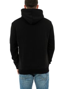 Zwarte hoodie met een kap, vanuit de achterkant gezien. Gemaakt van zacht materiaal, heeft ribgebreide manchetten en een zoom, gedragen over lichtblauwe jeans.