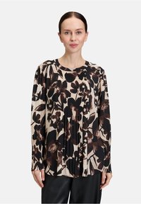 Blusa a maniche lunghe con motivo floreale in nero e marrone su sfondo beige chiaro, con texture plissè e scollo rotondo.