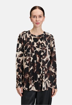 Blusa a maniche lunghe con motivo floreale in nero e marrone su sfondo beige chiaro, con texture plissè e scollo rotondo.