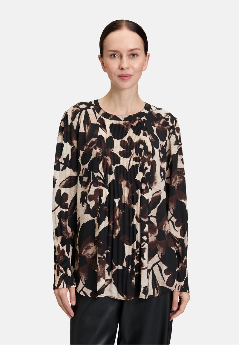 Blusa a maniche lunghe con motivo floreale in nero e marrone su sfondo beige chiaro, con texture plissè e scollo rotondo.
