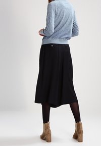 Vaaleansininen neulottu neule, jossa on tekstuurikuvio, yhdistetty mustaan lyhyeen hameeseen. Asusteena on beige nilkkapohjallinen saapas.