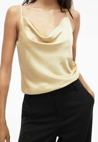 Pehmeas beežis satiinist kaminõlva, millel on õhukesed rihmad ja lõtv istuvus, kombineeritud kohandatud mustade pükstega. Sile tekstuur.