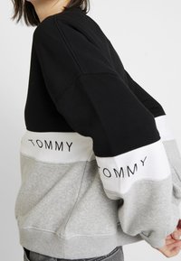 Sudadera con bloques de color en mezcla de algodón negro, gris y blanco. Presenta puños y bajo de canalé. Logo "TOMMY" impreso en la banda blanca.