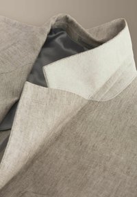 Bézs halszálkamintás gyapjúszövetből készült blézergallér, belső szürke béléssel és krémszínű galléralatti részlettel.