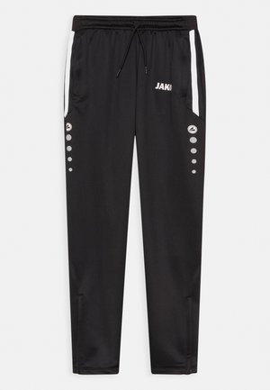 Pantalon de sport noir avec taille élastique à cordon de serrage, poches latérales, accents blancs et détails circulaires gris le long des jambes extérieures. Présente le logo "JAKO".