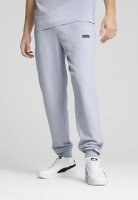 Helle graue Sweatpants aus weichem Stoff, mit elastischem Bund und Bündchen. Schwarzes "PUMA"-Logo auf der linken Hüfte. Weiße Sneakers mit schwarzen Akzenten.
