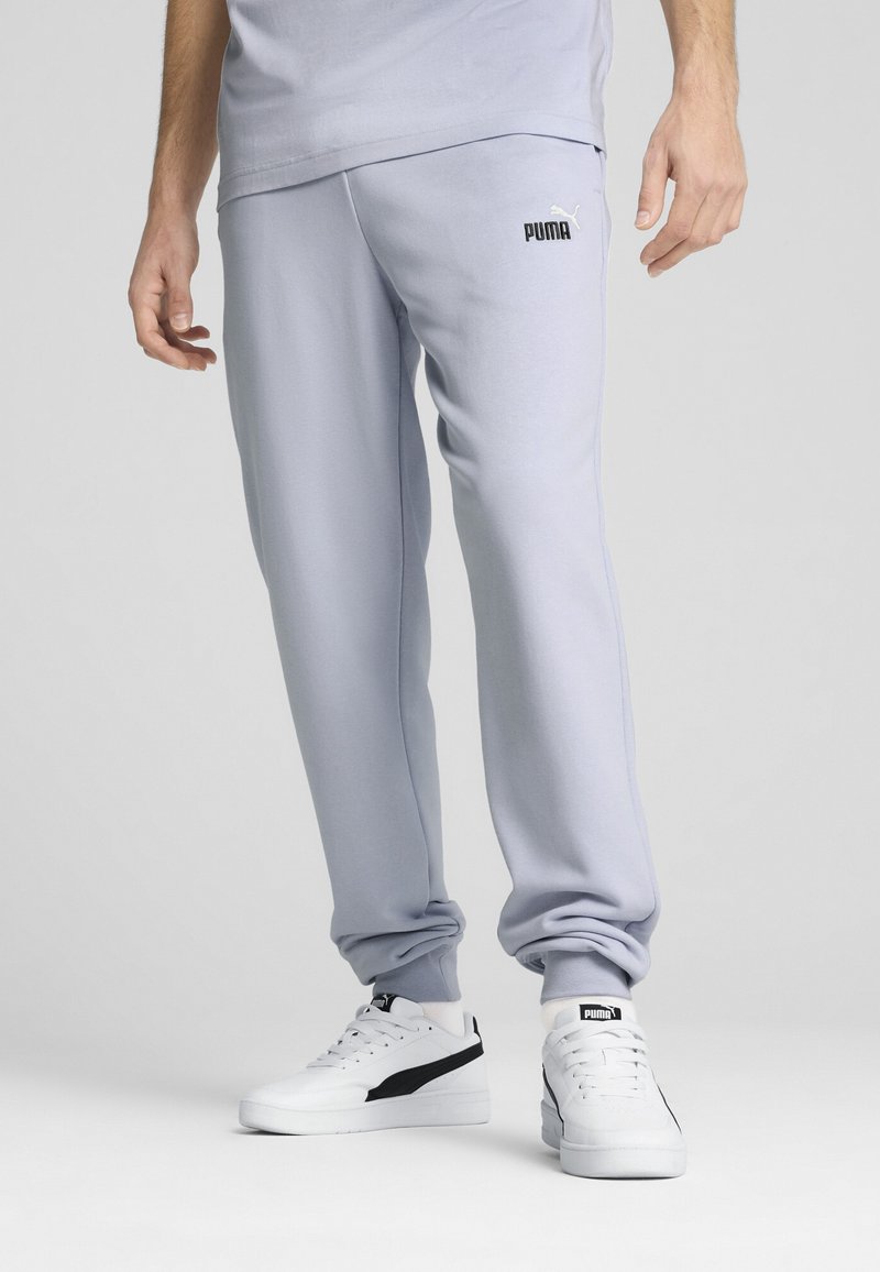 Helle graue Sweatpants aus weichem Stoff, mit elastischem Bund und Bündchen. Schwarzes "PUMA"-Logo auf der linken Hüfte. Weiße Sneakers mit schwarzen Akzenten.