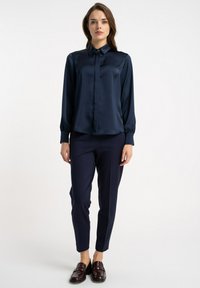 Granatowa satynowa bluzka z kołnierzykiem, długimi rękawami i ozdobnymi guzikami. Dopasowana do niej granatowe spodnie i ciemne mokasyny.