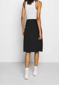 Black A-line skirt made of soft fabric, mid-calf length, featuring a smooth waistband. Styled with white sneakers and ankle socks.