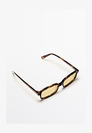 Occhiali tartaruga marroni con lenti rettangolari. Le lenti sono di un colore giallo, con una finitura lucida e aste sottili e dritte.