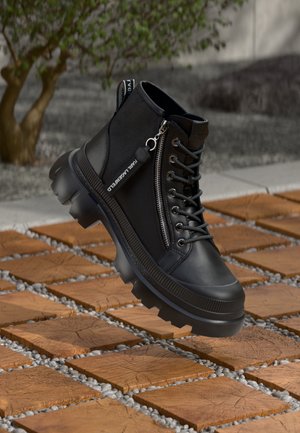 Black ankle boots made of synthetic material, featuring a side zipper, laces, and thick, rugged soles. Textured finish and contrasting accents.