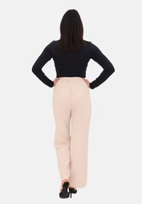 Maglietta nera a maniche lunghe abbinata a pantaloni palazzo rosa chiaro con vita elastica. Il modello indossa scarpe col tacco nere.