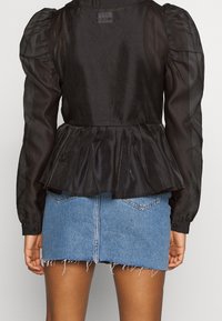 Blusa peplum nera con maniche puff e una trama trasparente, abbinata a una mini gonna in denim blu con orlo sfilacciato e tasche posteriori.