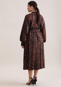 Abito a stampa leopardata in marrone scuro e nero, realizzato in tessuto morbido, caratterizzato da lunghe maniche a palloncino e una vita affusolata, lungo fino alla caviglia.
