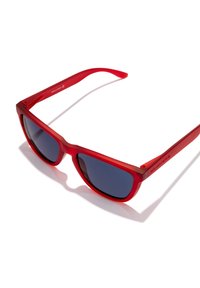 Rdeča plastična sončna očala z temno obarvanimi lečami, pravokotnim okvirjem in gladko teksturo; na strani je napisano ime blagovne znamke.
