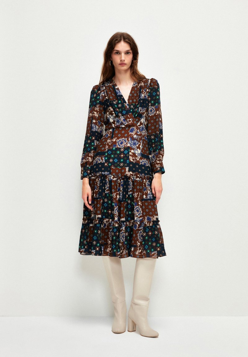 Vestido de manga larga y cruzado con una base marrón y patrones florales y geométricos en azul, verde y blanco, falda acampanada con volantes en capas y un escote en V profundo.