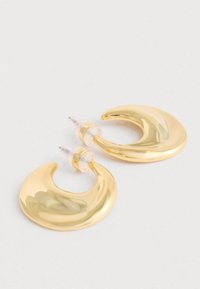 Pár lesklých zlatých náušníc v tvare polmesiaca so štrasovými plastovými zátkami na svetlom pozadí.