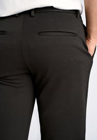 Pantaloni neri su misura realizzati in tessuto liscio, con davanti piatto, due tasche posteriori e un design slim fit.