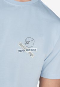 Camiseta de algodón azul claro con un gráfico de calavera y huesos cruzados, y el texto "HARPER AND NEYER" en colores contrastantes.