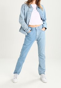 Giacca di jeans azzurro chiaro e jeans abbinati, peso medio, vestibilità rilassata, abbinati a un top corto bianco e sneakers bianche.