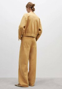 Bež jakna oversized kroja i široke hlače izrađene od pamučnog materijala, s elastičnom gumom u struku i stražnjim džepovima na hlačama.