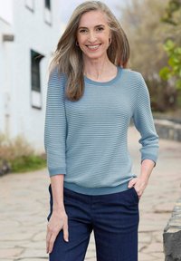 Hellblau gestreifter Strickpullover mit rundem Halsausschnitt und Dreiviertelärmeln, kombiniert mit dunkelblauen Hosen.