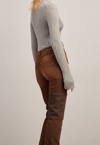 Top de manga larga gris acanalado combinado con jeans ajustados marrones que presentan un parche contrastante en la rodilla y detalles de costura resaltados.