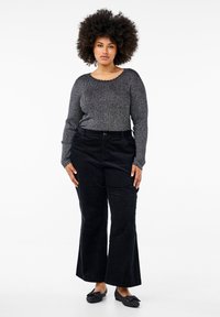 Svarta manchesterbyxor med vida ben, tillsammans med en texturerad mörkgrå långärmad topp med en vågig halsringning. Svarta slip-on skor.