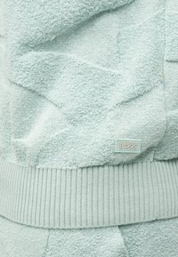 Φωτεινό γαλάζιο υφασμάτινο ύφασμα με μοτίβο αστεριών και μικρή ορθογώνια ετικέτα "BOSS" κοντά σε ριμπ πλέξη στο τελείωμα.