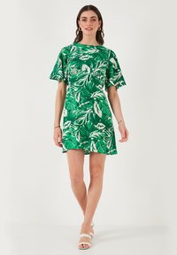 Vihreä mekko, jossa on valkoisia lehtikuvioita, lyhyet hihat ja rento leikkaus, pyöreä pääntie ja levenevä helma.